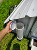 Person holding a lid to a white container for chicken feeder on a portable metal chicken coop on grass