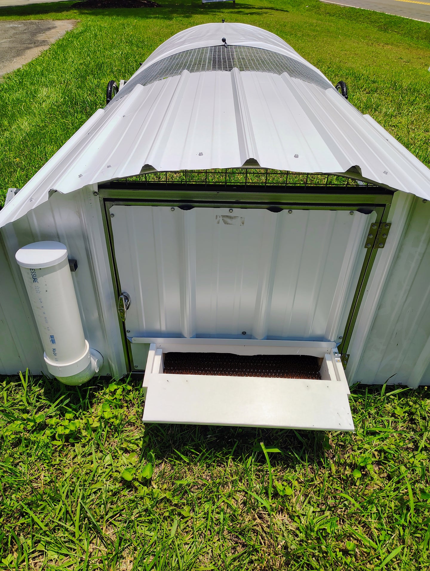 Metal chicken coop with open door on grass